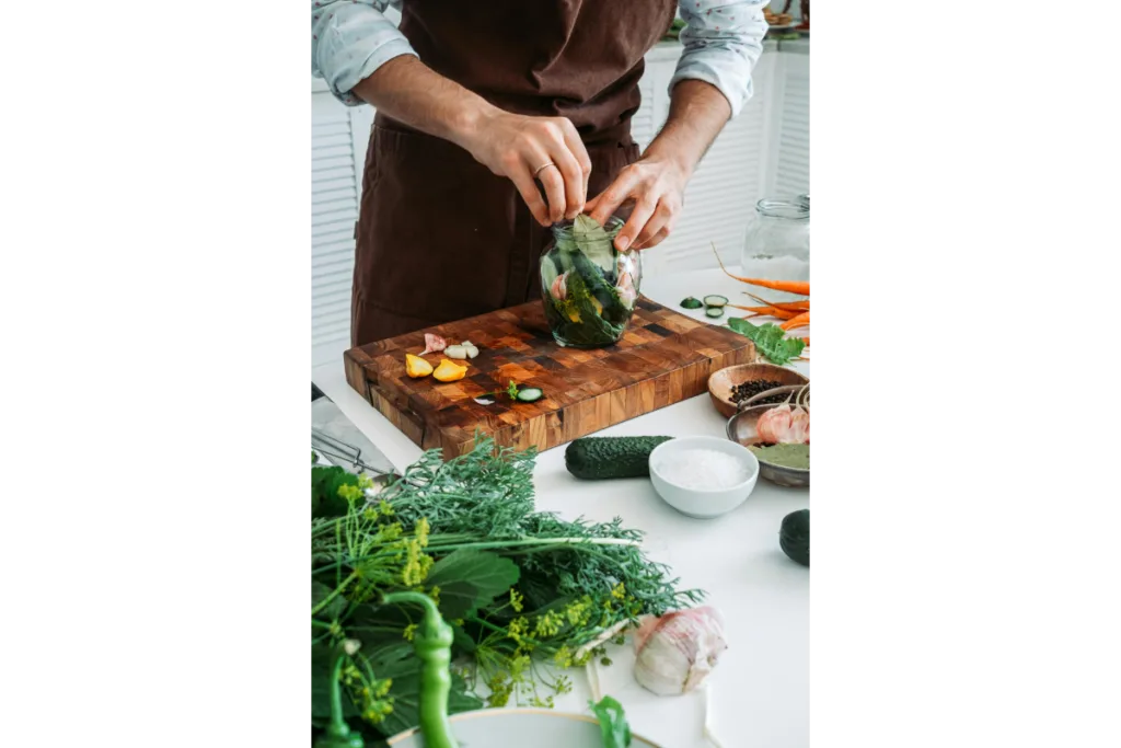 A man putting herbs in a glass jar.