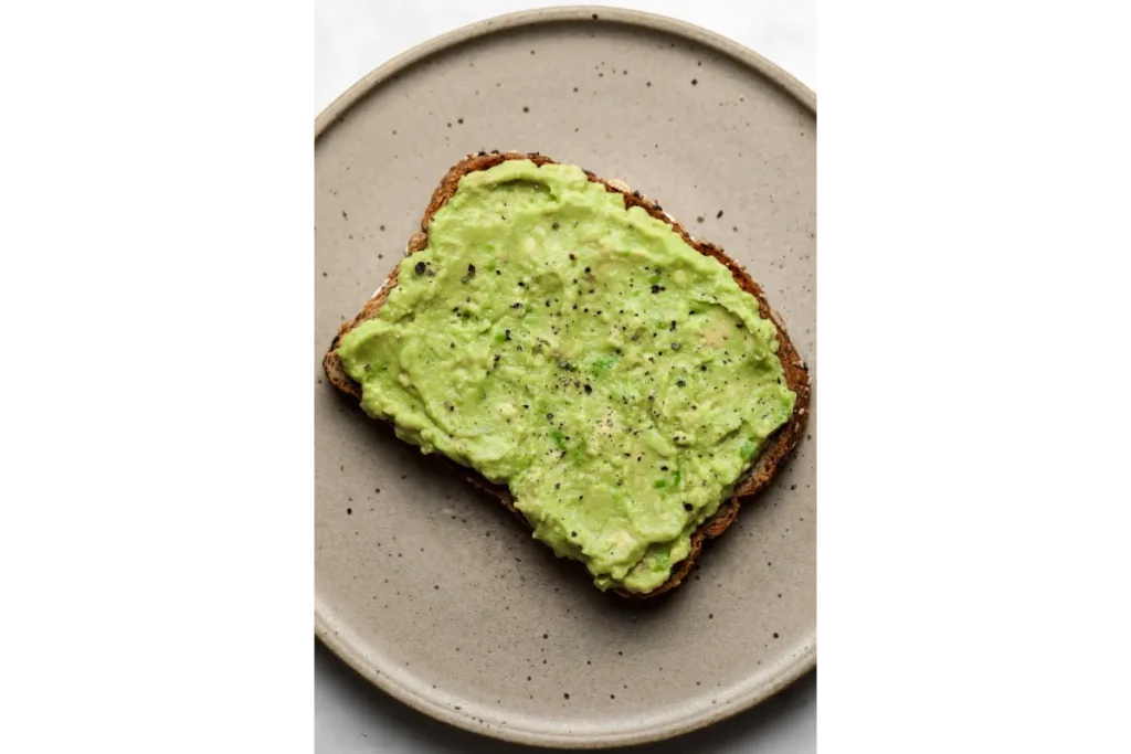 Avocado spread on a toasted bread placed on a grey plate with a white background - avocado toast recipe