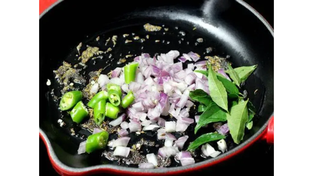 Poha being lightly sautéed in a pan with mustard seeds and onions.