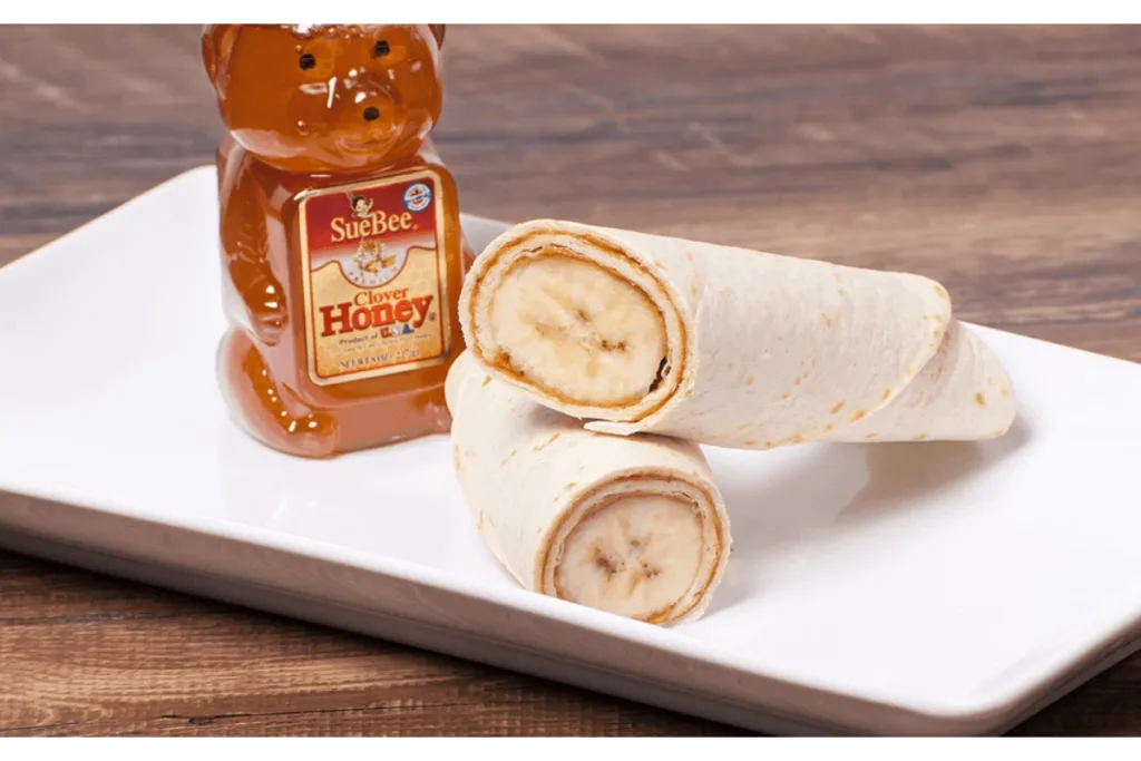 banana peanut butter wrap on a plate with a bottle of honey beside it