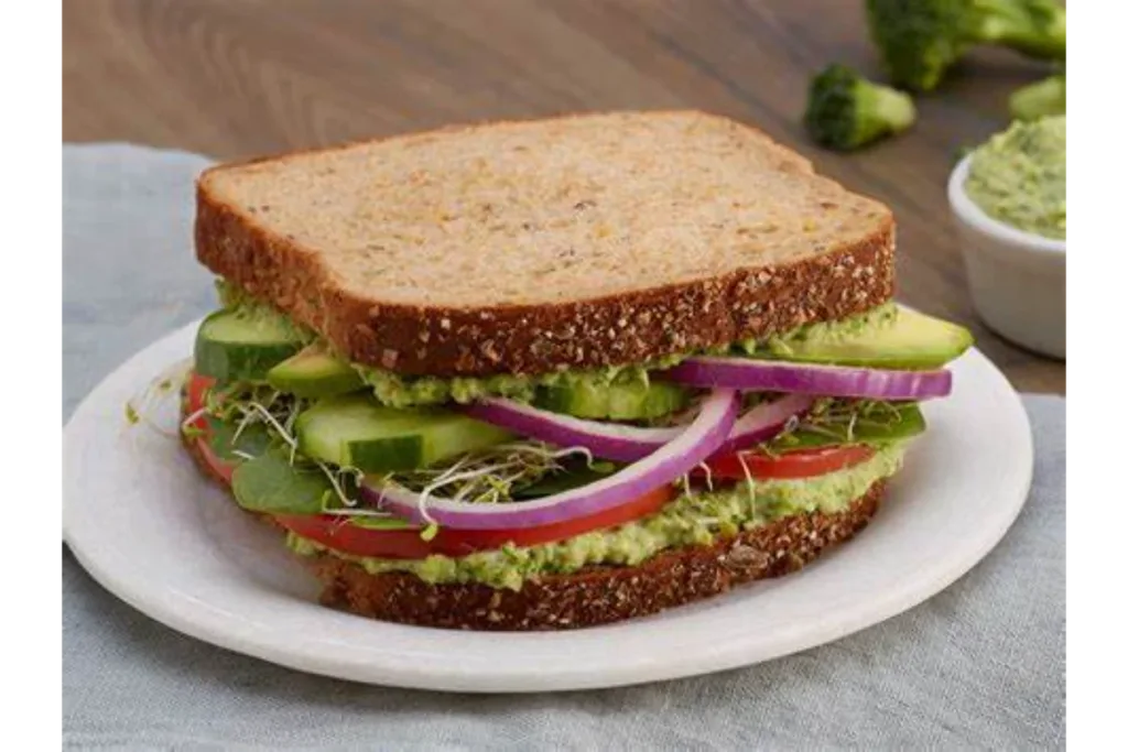 avocado sandwich on a white plate placed on a grey cloth on a wooden table.