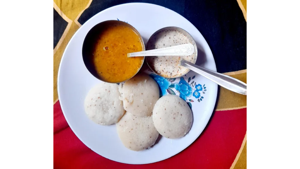 A plate of steamed idlis served with creamy coconut chutney and spicy sambar.